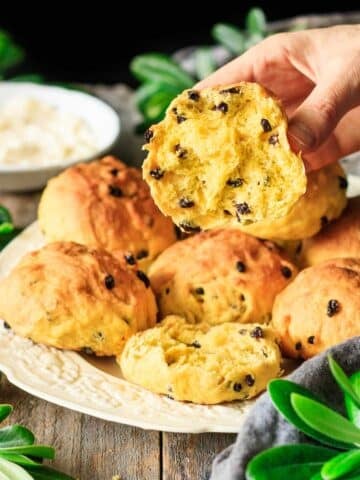 holding half of a Cornish saffron bun split lengthwise.