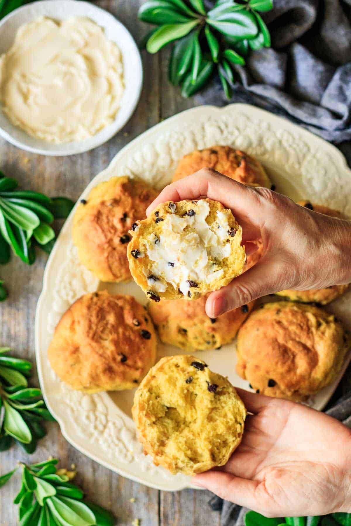 person holding a halved Cornish saffron bun with butter spread on one piece.