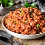 bowl of baked beans with two black spoons and a gray piece of fabric.