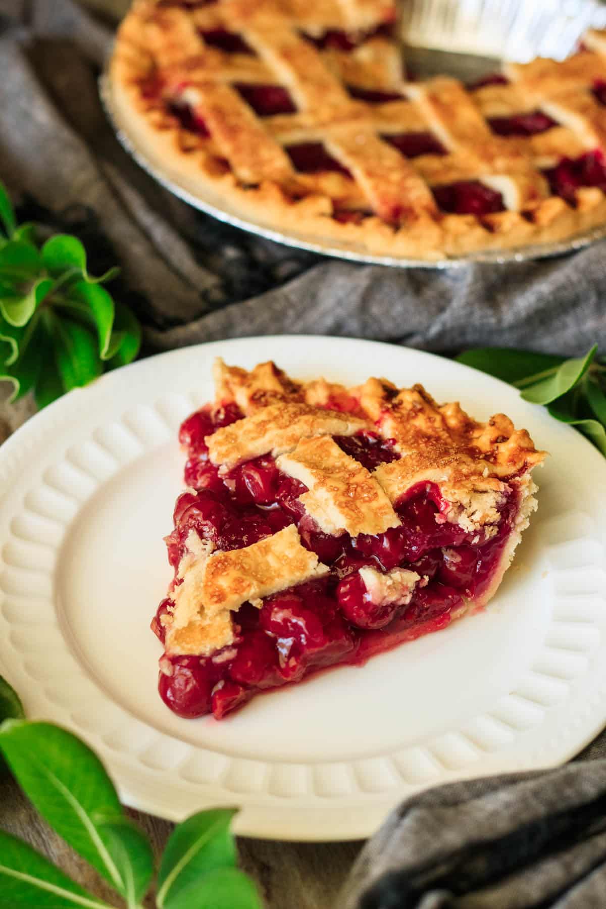 slice of cherry pie with a lattice-topped pie in the background.