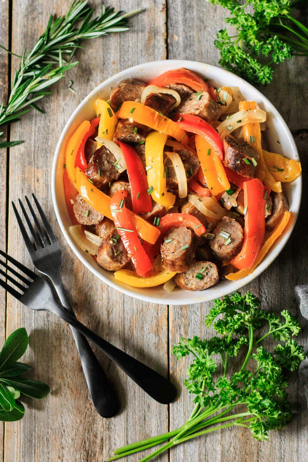 bowl of sausage, peppers, and onions with two black forks.