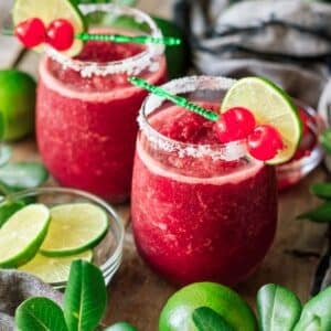 two glasses of frozen cherry limeade with a bowl of lime wheels.
