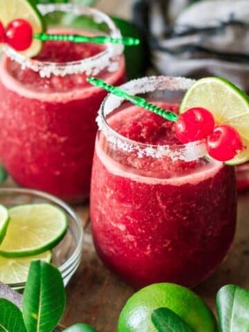 two glasses of frozen cherry limeade with a bowl of lime wheels.