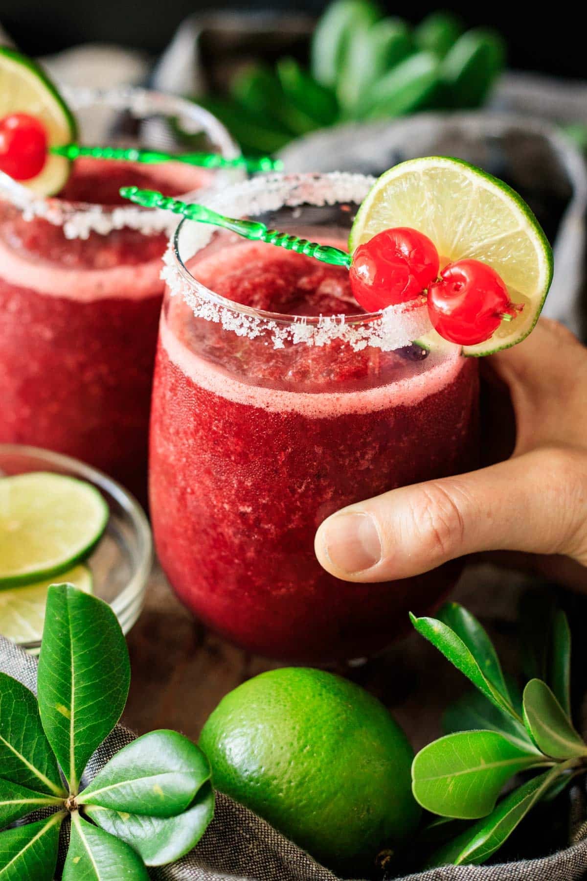 person holding a stemless wine glass of frozen cherry limeade.