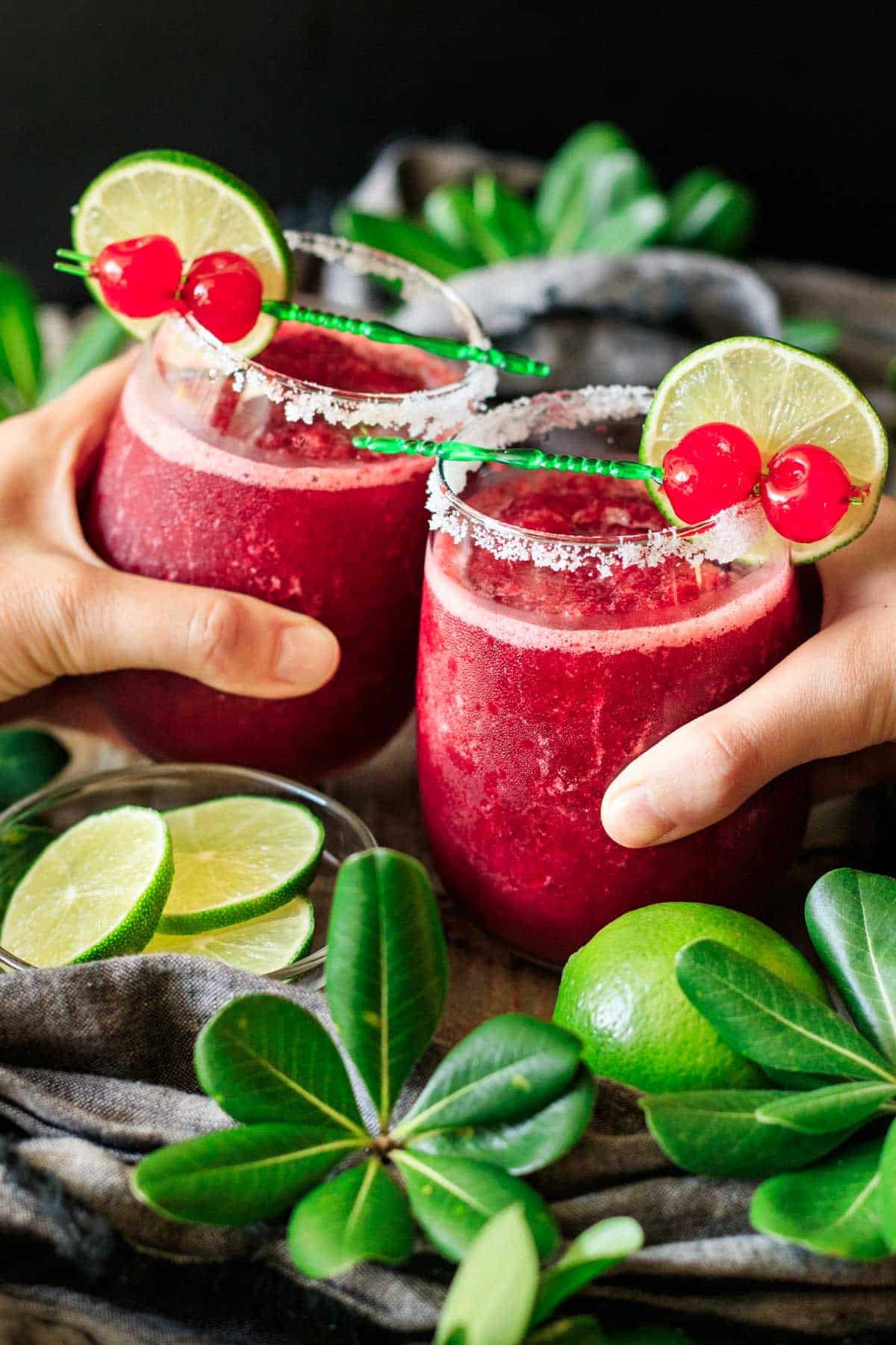 people doing a toast with two glasses of frozen cherry limeade.