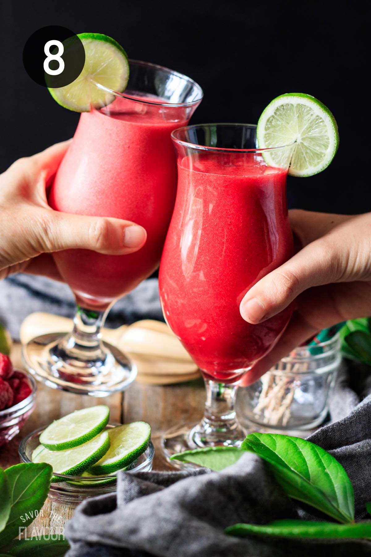 people doing a toast with two raspberry daiquiris in hurricane glasses.
