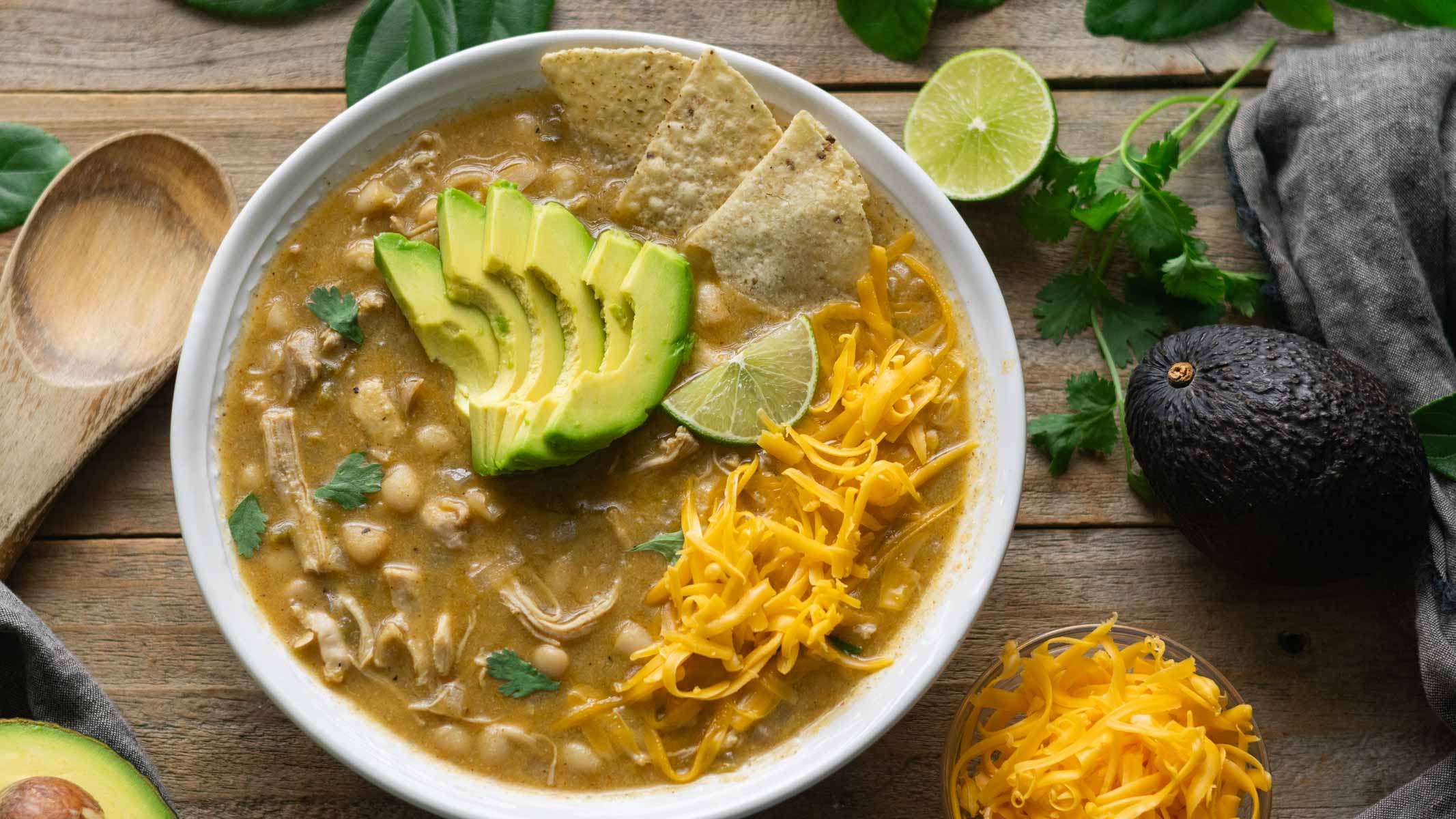 large white serving bowl of white chicken chili with avocado and grated cheese.